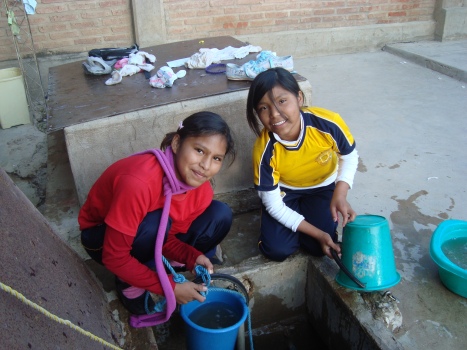 Two of the middle school aged girls are taking water out of the well to wash their clothes.
